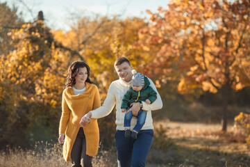 Fototapeta premium a young man, a woman and their little boy walk through the forest in autumn holding hands