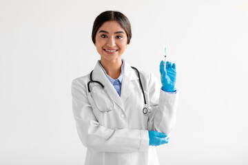 Smiling young hindu female medical worker in uniform, protective gloves, shows syringe with vaccine