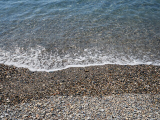 Background of a pebble beach with clean transparent water and foam in the Mediterranean sea. La Herradura, province of Granda, Spain