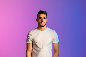 Portrait of handsome young middle Eastern man having serious face expression, wearing casual clothes in neon light