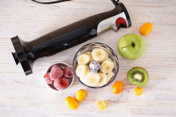 Hand blender and accessories with sliced fruit on a wooden background. Flat lay.