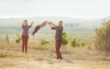 a young woman and a man with a little boy  are standing in a vineyard,  they're having fun,  they throw up their son, play with him. They are wearing plaid shirts..