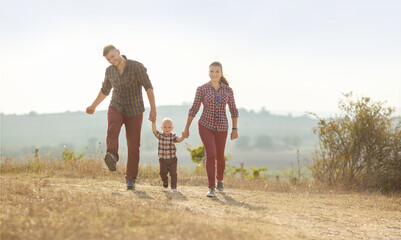 a young woman , a man and a little boy are having fun holding hands in a vineyard . They are dressed in plaid shirts