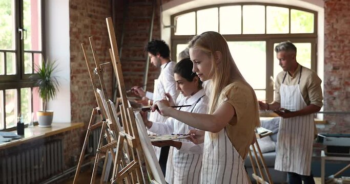 Painting class. People of diverse age gender racial ethnic groups attend lesson at art studio engaged in oil painting using brushes palettes. Drawing school students stand by easels work on pictures
