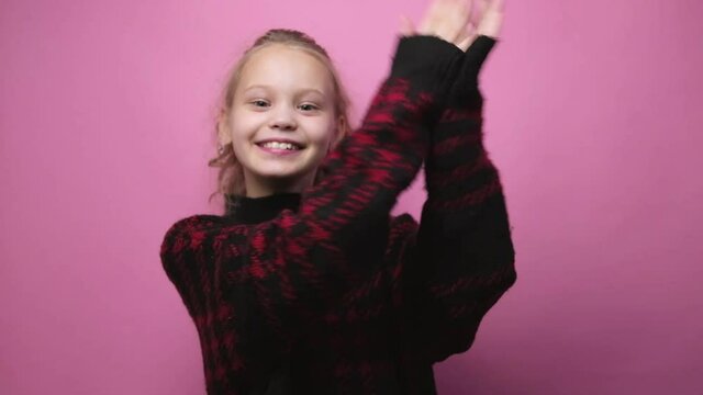 Happy smiling little girl dancing on pink background. Dancing kid having fun performing freestyle dance.