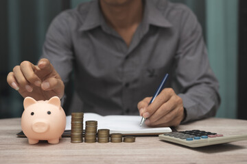 saving money and accounting concept. business man putting coin insert to piggy bank and make acounting book for finance management to investment and saving.
