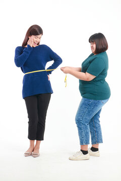 Fat Asian woman holding a tape measure around her waist to measure waist circumference of skinny women Check her waist size to help plan for weight gain or weight loss. Concept of health care. Dress.