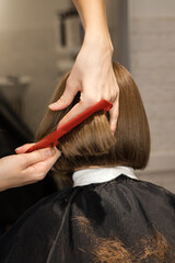 Closeup back view of preteen girl sitting in chair in hair salon. hairdresser checking her new...