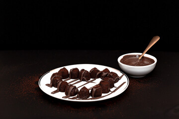 Chocolate truffles are laid out in the shape of a heart and poured with chocolate on a white porcelain plate on a dark background. Selective focus