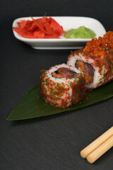roll with red caviar and fish near ginger and wasabi on a dark background