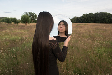 portarit of young asian woman in a field holding round mirror with her reflection