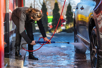 Young woman washing a car in a self-service car wash.