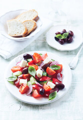 Simple salad with cherry tomatoes, feta cheese, kalamata olives, red pepper and fresh herbs. Bright wooden background.