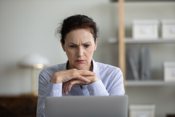 Fototapeta Unhappy middle aged woman looking at computer screen, feeling stressed reading email with bad news, stack with difficult task, considering problem solution online at home office, working distantly. obraz