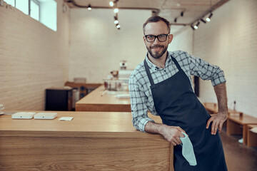 Cheerful cafe owned standing by wooden counter