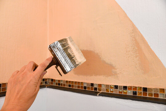 Woman's hand with a paintbrush, repaints the corner of the wall with terracotta paint