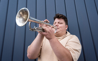 Young street musician playing the trumpet near the big blue wall