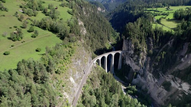 Landwasser Viaduct in the Swiss Alps in summer, Aerial view. Panoramic view of a green mountain valley. Famous viaduct in a mountain gorge. Glacier Express in Switzerland, Graubunden, Bernina pass. 4K