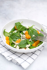 Healthy and light salad of spinach, tangerines and gorgonzola in white plate on the napkin for snack. Healthy food. Vegetarian food. Grey background.