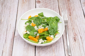 Healthy and light salad of spinach, tangerines and gorgonzola in white plate for snack. Healthy food. Diet food. Wooden background.