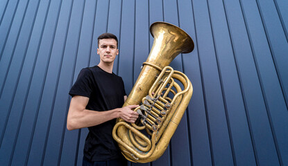 Young street musician playing the tuba near the big blue wall