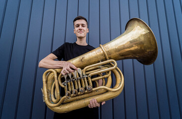 Young street musician playing the tuba near the big blue wall