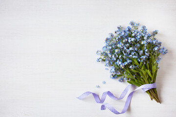 Bouquet of spring flowers forget-me-nots with ribbon on light wooden background - 479355492