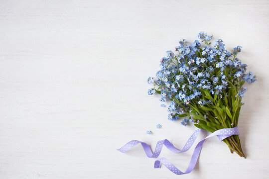 Bouquet of spring flowers forget-me-nots with ribbon on light wooden background