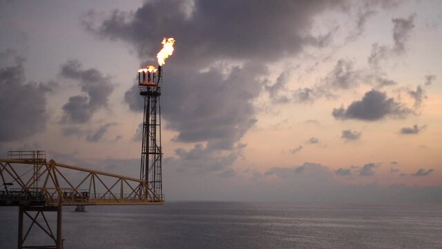 Slow motion of flare burning bridge of oil and gas platform or offshore platform with sun rise and beautiful clouds in the sea for oil and gas industry concept.