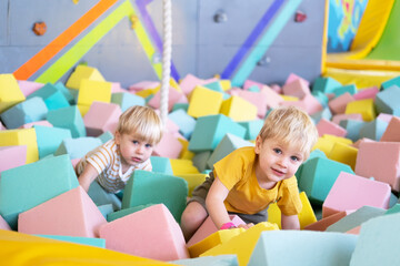 two cute little boys twins plays with soft cubes in the dry pool in play center