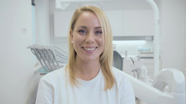 Portrait of a young happy Caucasian woman with a bright smile and white teeth, standing at a dental office.