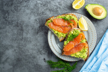 Toasts with avocado and smoked salmon on gray background, copy space. Healthy food.