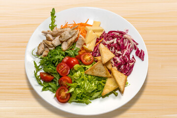 Caesar salad with chicken, cheese, tomato and croutons in white plate on wooden background