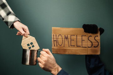 A man hold a cardboard sign with the inscription HOMELESS and steel cup. Woman put a carved mini...