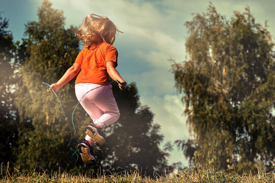 Child Jumping Rope In The Park On A Sunny Day. A Ten-year-old Girl Goes In For Outdoor Sports In The Summer.