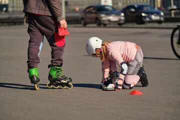A ten-year-old girl trains on the street to roller skate with a coach. The child goes in for sports...