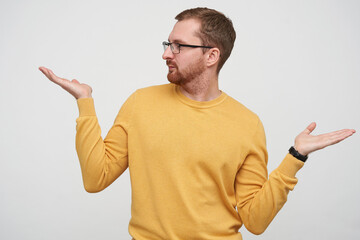 Studio portrait of young bearded male student wears yellow sweater looks aside at copy space, trying to make a choice, feels confused, isolated over white background