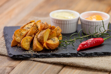 pedaços de batata rústica servida em pedra de ardósia com ramequin com molho e alecrim com pimenta vermelha sobre tecido juta e madeira