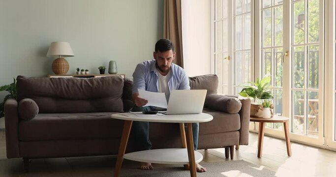 Serious millennial man self employed entrepreneur freelancer study contract agreement draft think on terms conditions plan investment. Young businessman work with papers at cozy home office on weekend