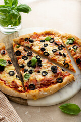 Homemade pizza ham, black olives, cheese and fresh basil. Sourdough pizza.