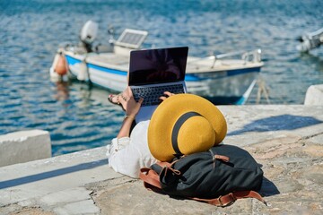 Woman in hat typing on laptop, water bay boat background