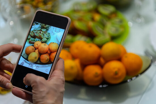 Hands take pictures on smartphone of plate with oranges.
