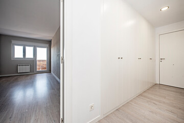 Corridor with a wall full of white cabinets and entrance to a living room with a terrace