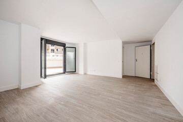 Unfurnished living room with white painted walls with ceramic tile floors, front door and large window that opens onto a patio