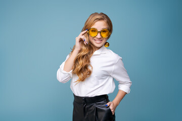 Cheerful young woman wearing yellow glasses smiling at camera against blue background. Close up happy teenage boy laughing with glasses. Beautiful girl having fun with cute eyes, showing big grin