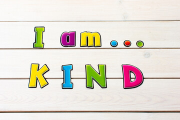 I am kind. Positive affirmation, statement. Bold neon letters on white washed pine table.