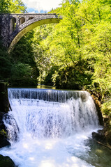 Waterfall with a stone bridge in the narrow gorge of Vintgar in Slovenia. Natural protected area deep canyon among the rocks with a wild river.