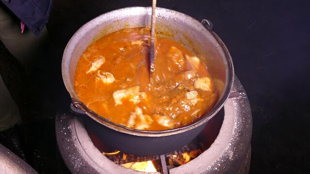 Goulash is prepared with seasoning and meat. Steam from a hot dish. Kitchen in a cauldron. Stir with a kitchen spatula. Campfire food.