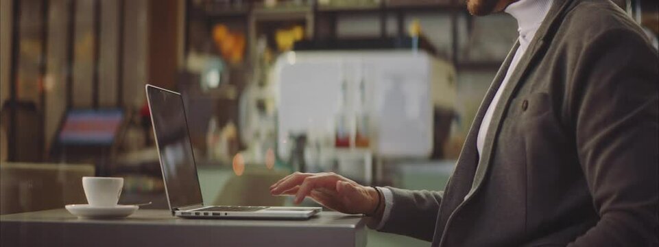 Cropped shot of man operating modern laptop computer by one hand.  Sitting in evening in cafe. Entrepreneur working outside office.