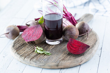 A tall glass of beet juice surrounded by whole and cut beets.